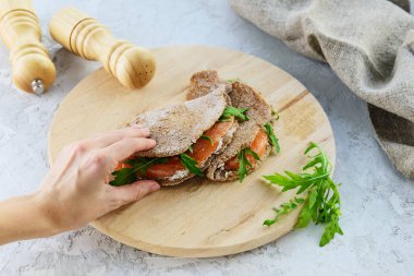 Bir el, ahşap bir tahtanın üzerinde balık, ot ve keçi peynirli çavdar tortilla istiyor. Glütensiz, düzgün beslenme..