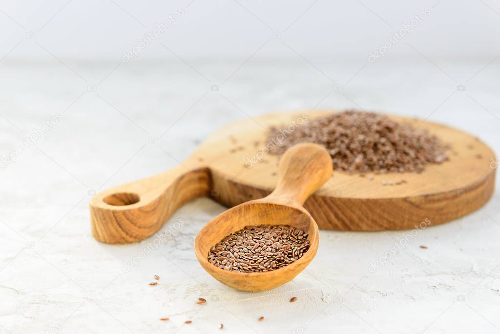 Flax seeds in a wooden spoon and board on a gray background.