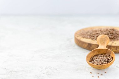Tahta bir kaşıkta keten tohumu ve gri bir masada yemek. Yatay yönelim, boşluğu kopyala.