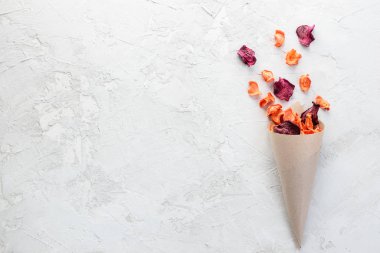 Gri bir masada kağıt torbada pancar ve havuç cipsi. Yatay yönelim, üst görünüm, kopyalama alanı.