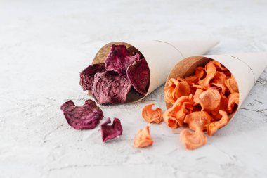 Gri bir masada kağıt torbalarda havuç ve pancar cipsi..