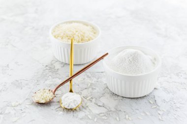 Gri arka planda pirinç unu ve pirinç kaseleri. Glütensiz, sağlıklı beslenme konsepti.