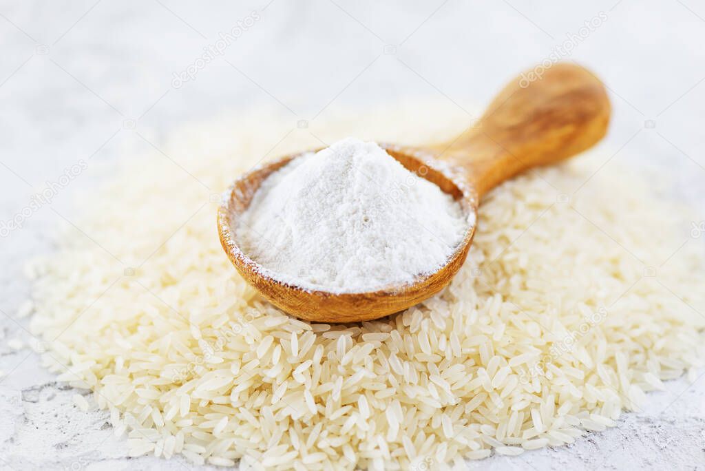 Rice flour in a wooden spoon on a pile of white rice. Gluten free, healthy diet concept.