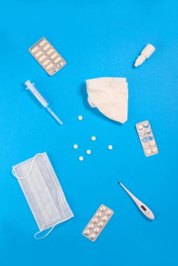 Tıbbi maskesi, şırıngası, termometresi ve mendili olan antiviral ilaçlar. Dikey yönelim, üst görünüm.