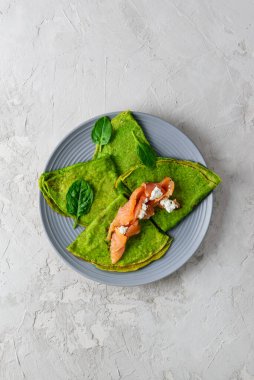 Gri tabakta somon ve süzme peynirli ıspanaklı krep. Dikey yönelim, üst görünüm.