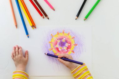 Bir çocuk bir kağıt parçasına covid-19 virüsü çiziyor. Karantina sırasında evde eğitim. Yatay yönelim, üst görünüm.