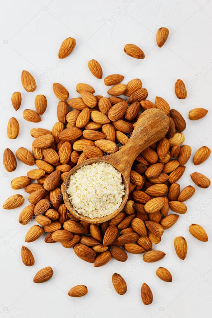 Almond flour in a wooden spoon on a background of almonds. Vertical orientation, top view. Healthy food, gluten free.