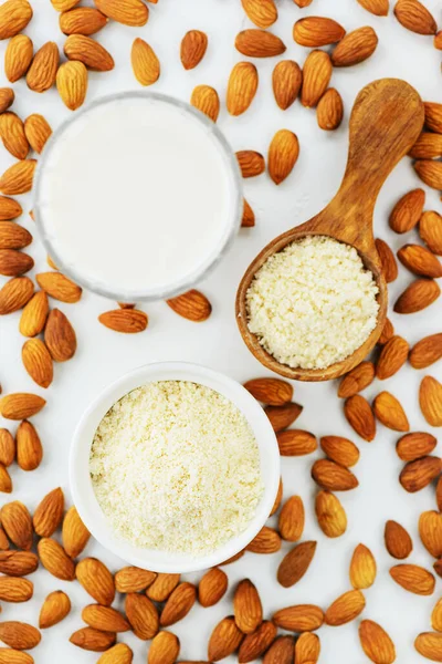 Almond flour in a spoon and bowl with a glass of almond milk on a background of almonds. Healthy food, gluten free. Vertical orientation, top view.