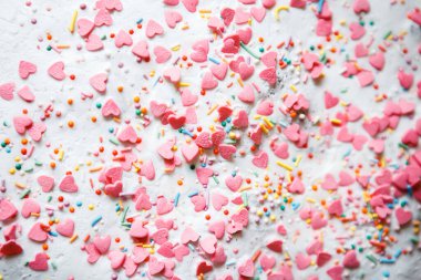 On a white sugar backing lies a sweet pastry topping in the form of pink hearts, orange, turquoise and red peas, and green, blue and yellow sticks