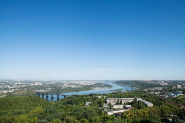 Şehrin üst manzarası, nehrin kıvrımı, köprü, konut binaları ve yeşil bir sıra ağaç. Mavi gökyüzü. Yatay çerçeve.