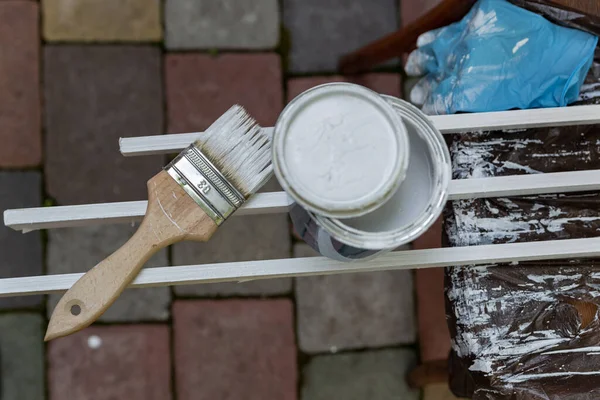 paint brush covered with white paint and a jar of paint painted strips on a dark background