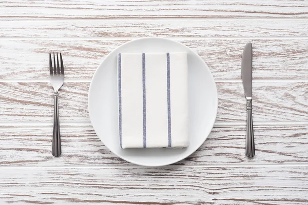 Plato vacío servilleta tenedor cuchillo plata fondo de mesa de madera blanca — Foto de Stock