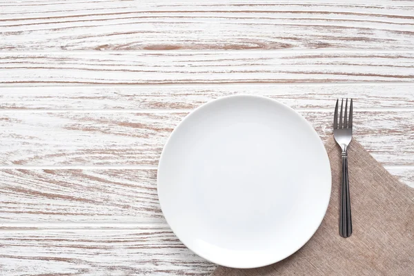 Assiette vide serviette fourchette argenterie blanc fond de table en bois — Photo