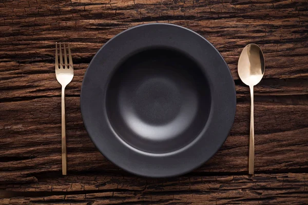 Cucchiaio forchetta piatto ciotola nero su sfondo tavolo di legno — Foto Stock