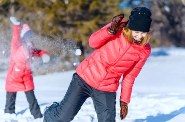 Açık parlak ceket oynarken, iki genç kız portresi bir kış parkta snowballs. Eğleniyor kar fırlatma