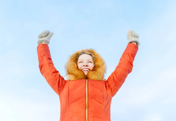 Outdoor Portret van een lachende meisje in de winter donsjack, verhogen hun handen tegen de blauwe hemel — Stockfoto