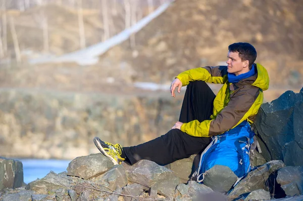 Un jeune homme avec un sac à dos assis sur le bord du lac d'automne — Photo