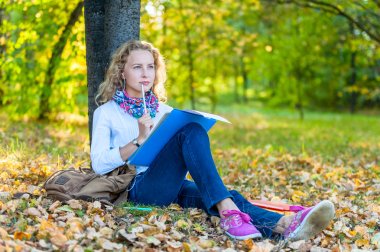 Düşünceli kız öğrenci oturur ve sonbahar parkta yazıyor