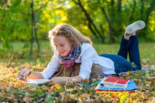 Dziewczyna student myślenia, leżącego na żółty autumn odchodzi i czytanie w parku jesień — Zdjęcie stockowe