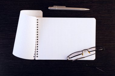 Defter, gözlük ve ahşap masa üzerinde kalem. Metin için yer. Kare görüntü.