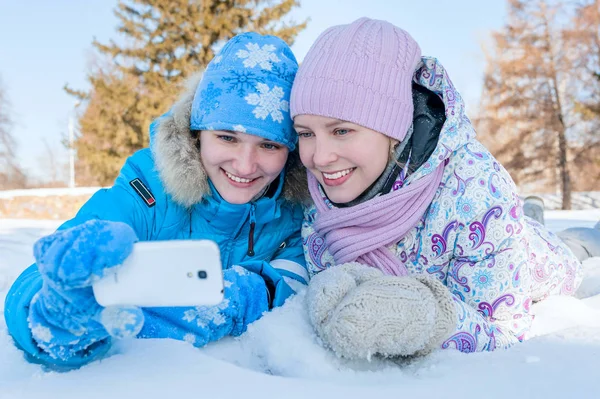 Selfie. Twee gelukkige lachende meisje liggend in de sneeuw in de winter park. Outdoor Portret — Stockfoto