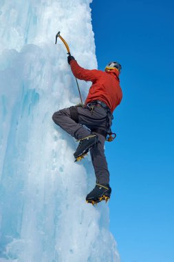 Elinde buz aletleri olan dağcı adam baltayla büyük bir buz duvarına tırmanıyor. Açık hava Spor Portresi