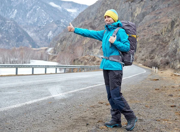 Una joven sonriente está viajando por las montañas. detiene el coche en la carretera (autoestop), levanta la mano — Foto de Stock