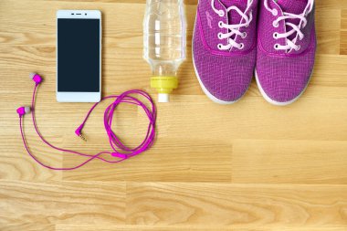 Fitness kavramı ile hareket eden telefon kulaklık, kadın spor pembe ayakkabı, şişe su, tahta arka plan ile çalıştırın