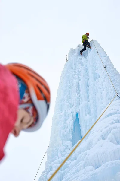 Elinde buz aletleri olan dağcı adam turuncu kasklı baltayla büyük bir buz duvarına tırmanıyor. Açık hava Spor Portresi — Stok fotoğraf
