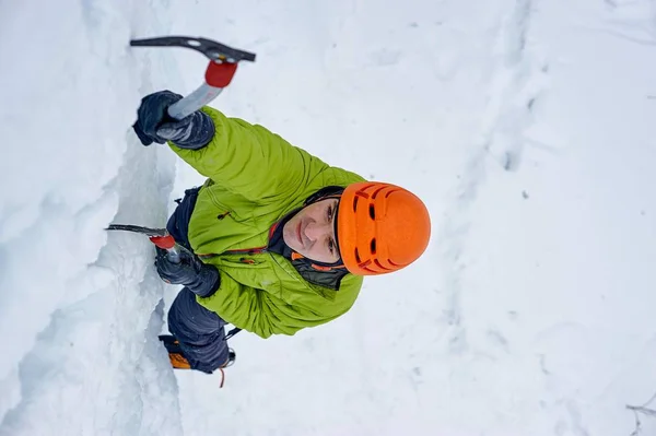 Uomo alpinista con piccozza in casco arancione arrampicata su una grande parete di ghiaccio. Sport all'aperto Portrai — Foto Stock