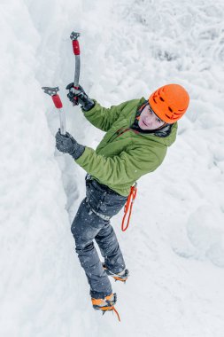 Elinde buz aletleri olan dağcı adam turuncu kasklı baltayla büyük bir buz duvarına tırmanıyor. Açık hava Spor Portresi