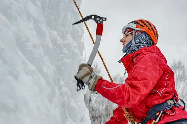 Donna alpinista con piccozza in casco arancione arrampicata su una grande parete di ghiaccio. Ritratto sportivo all'aperto — Foto Stock