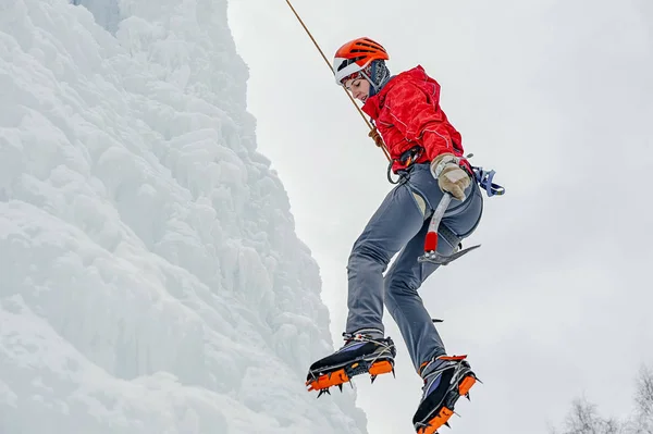 Femme alpiniste avec piolet à outils en casque orange escaladant un grand mur de glace. Portrait de sport extérieur. — Photo