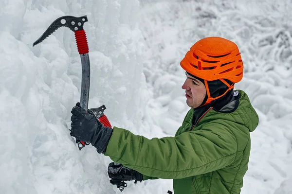 Homme alpiniste avec piolet à outils en casque orange escaladant un grand mur de glace. Portrait de sport extérieur. — Photo
