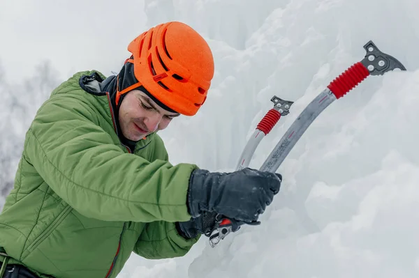 stock image Athletic alpinist man in orange helmet and ice tools axe climbing a large wall of ice. Outdoor Sports Portrait