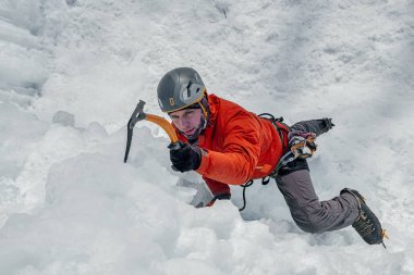 Elinde buz aletleri olan dağcı adam baltayla büyük bir buz duvarına tırmanıyor. Açık hava Spor Portresi