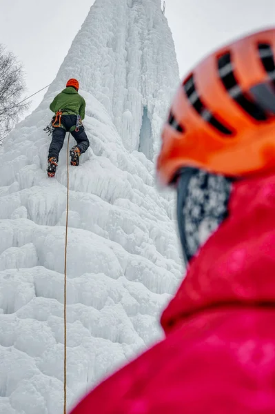 Homme alpiniste avec piolet à outils en casque orange escaladant un grand mur de glace. Portrait de sport extérieur — Photo