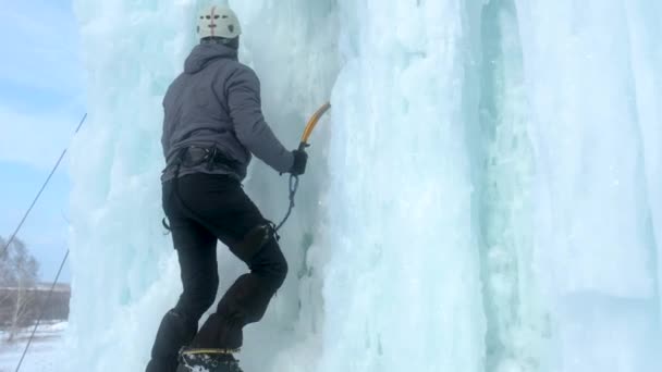 Alpinist man med is verktyg yxa klättra en stor vägg av is — Stockvideo
