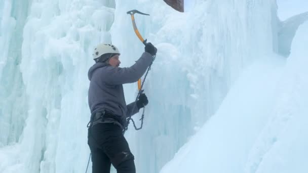 Alpinista ember jégcsákánnyal, aki egy nagy jégfalon mászik. — Stock videók