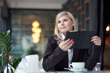 Kafede kitap okuyan ve kahve içen genç bir kadın.