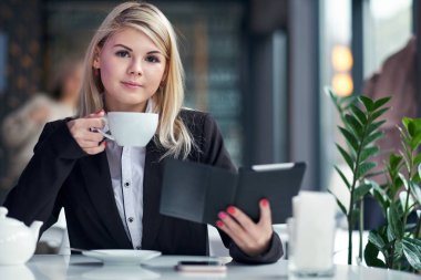 Kafede kitap okuyan ve kahve içen genç bir kadın.