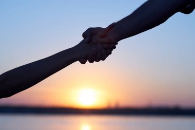 Yardım eli uzatıp. Siluet İki el, erkek ve kadın, gökyüzü gün batımında sıkı tutarak