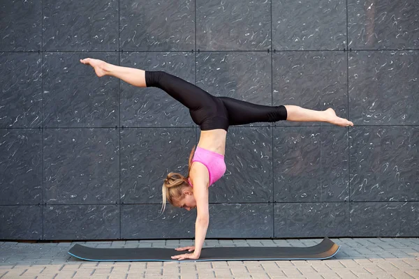 Mujer estirada. fitness o gimnasta o bailarina haciendo ejercicios handstand sobre fondo de uban de pared gris. Chica está de pie en sus manos —  Fotos de Stock