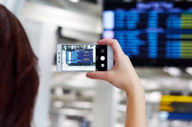 El havaalanında akıllı telefonda fotoğraf çeker. Ekranda, uçuş kalkış programı
