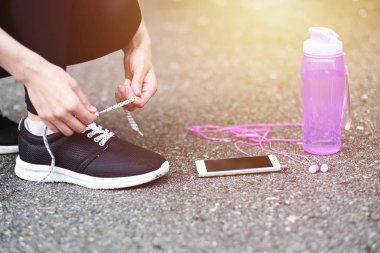 Koşu ayakkabısı bağlayan koşucu kadın koşuya hazırlanıyor stadyumda bir şişe su ve kulaklıkla koşuya hazırlanıyor.