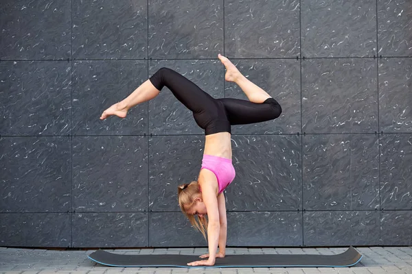 Mujer estirada. fitness o gimnasta o bailarina haciendo ejercicios handstand sobre fondo de uban de pared gris. Chica está de pie en sus manos —  Fotos de Stock