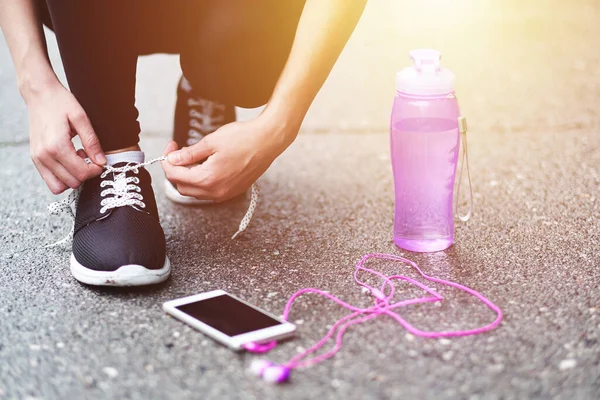Koşu ayakkabısı bağlayan koşucu kadın koşuya hazırlanıyor stadyumda bir şişe su ve kulaklıkla koşuya hazırlanıyor.
