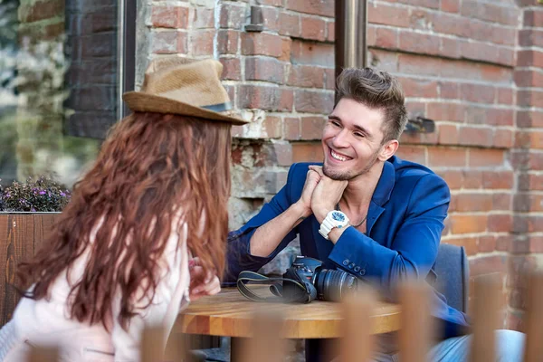 Casal sentado no outono no café na rua, uma parede de tijolo no fundo. Mulher de chapéu — Fotografia de Stock