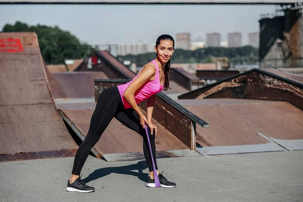Mulher fitness fazendo exercícios de alongamento com elástico elástico no fundo da cidade urbana — Fotografia de Stock