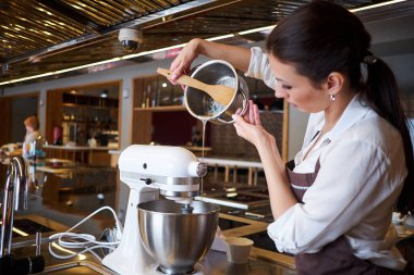 Önlüğüyle tezgahta duran bir kadın mikser kullanıyor. Pastadan tatlı yapmak.